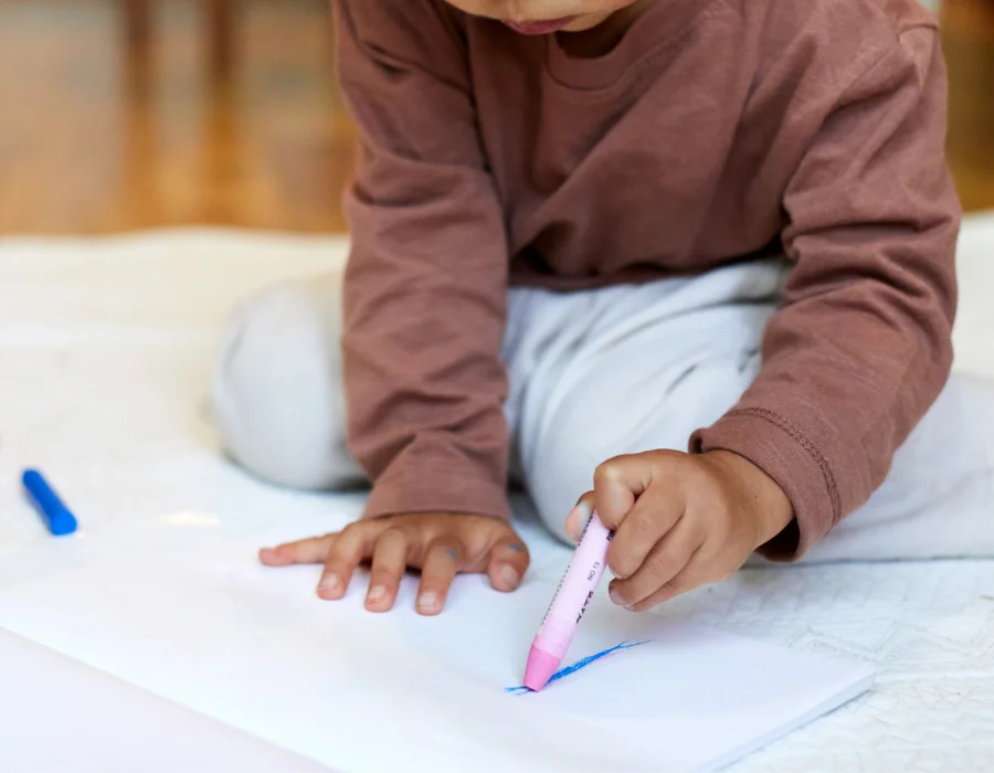 Young child gripping a marker awkwardly while drawing, an early sign of fine motor difficulty