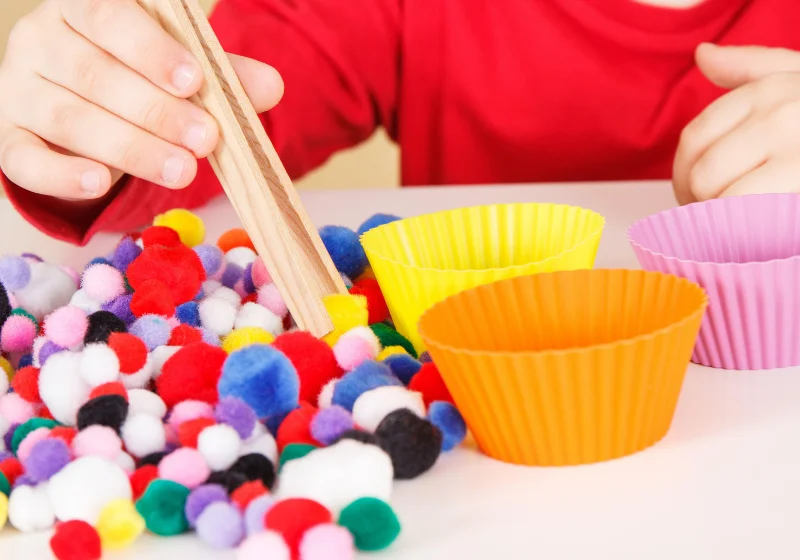 Child using tongs to sort pom-poms, a visual motor and hand coordination activity