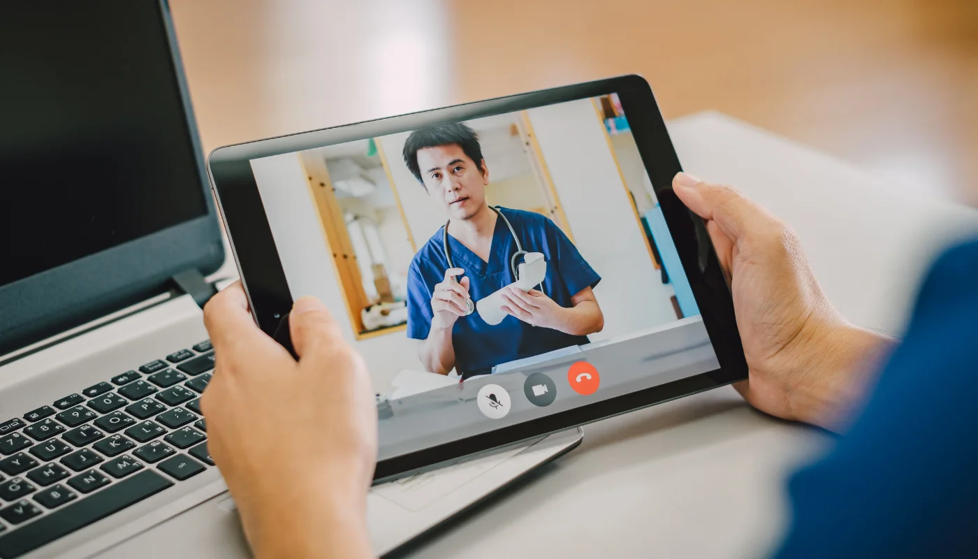 Patient joining an online physiotherapy consultation with a physiotherapist on a laptop and tablet video call