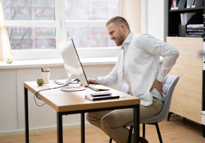 Busy professional with back pain at a desk preferring an at-home physiotherapy assessment