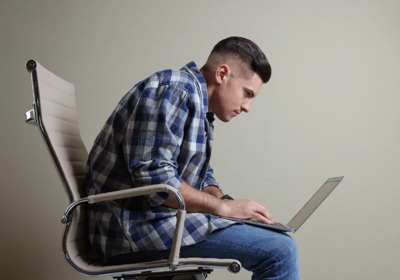Man slouched at a poorly set up home workstation needing postural and ergonomic advice