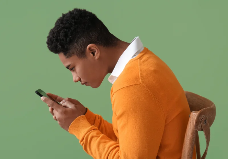 Young man with tech neck posture looking down at his mobile phone
