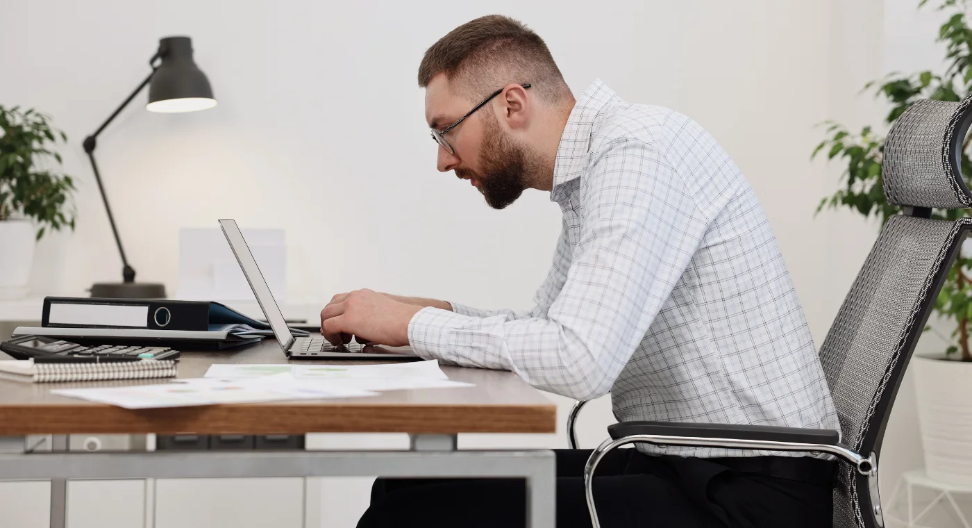 Office worker with forward head posture and rounded shoulders hunched over a laptop