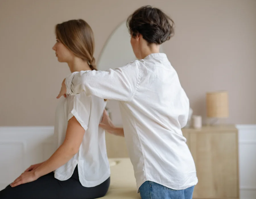 Physiotherapist checking spinal alignment and shoulder height during a static posture assessment